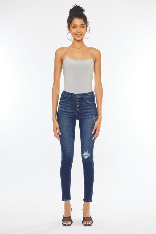 A woman in a gray tank top and High Rise Piecing Detail Super Skinny Jeans stands against a plain white backdrop while looking down and smiling. She is wearing black heeled sandals.