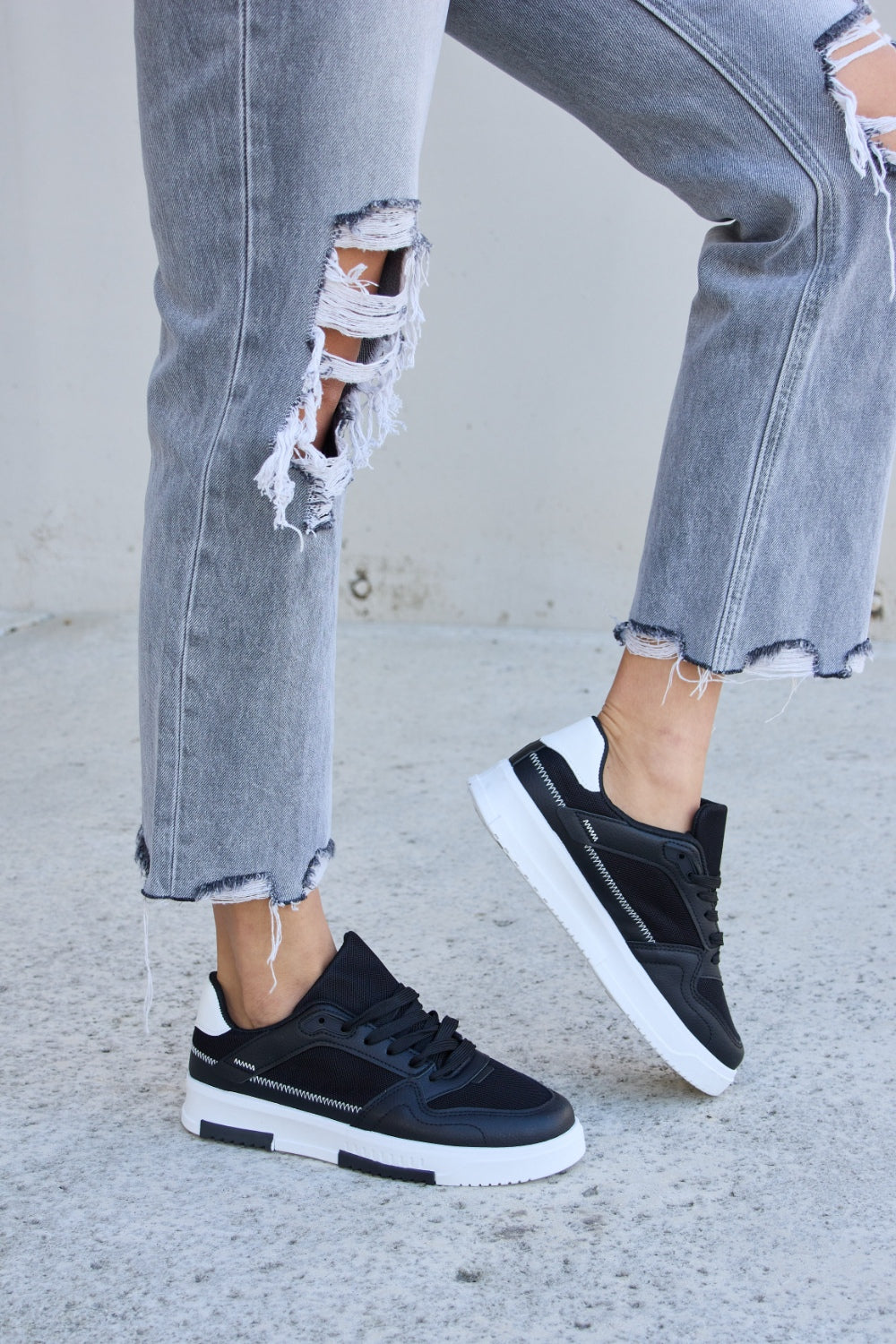 Forever Link Lace-Up Round Toe Flat Sneakers with white soles, styled with ripped gray jeans on a concrete surface.