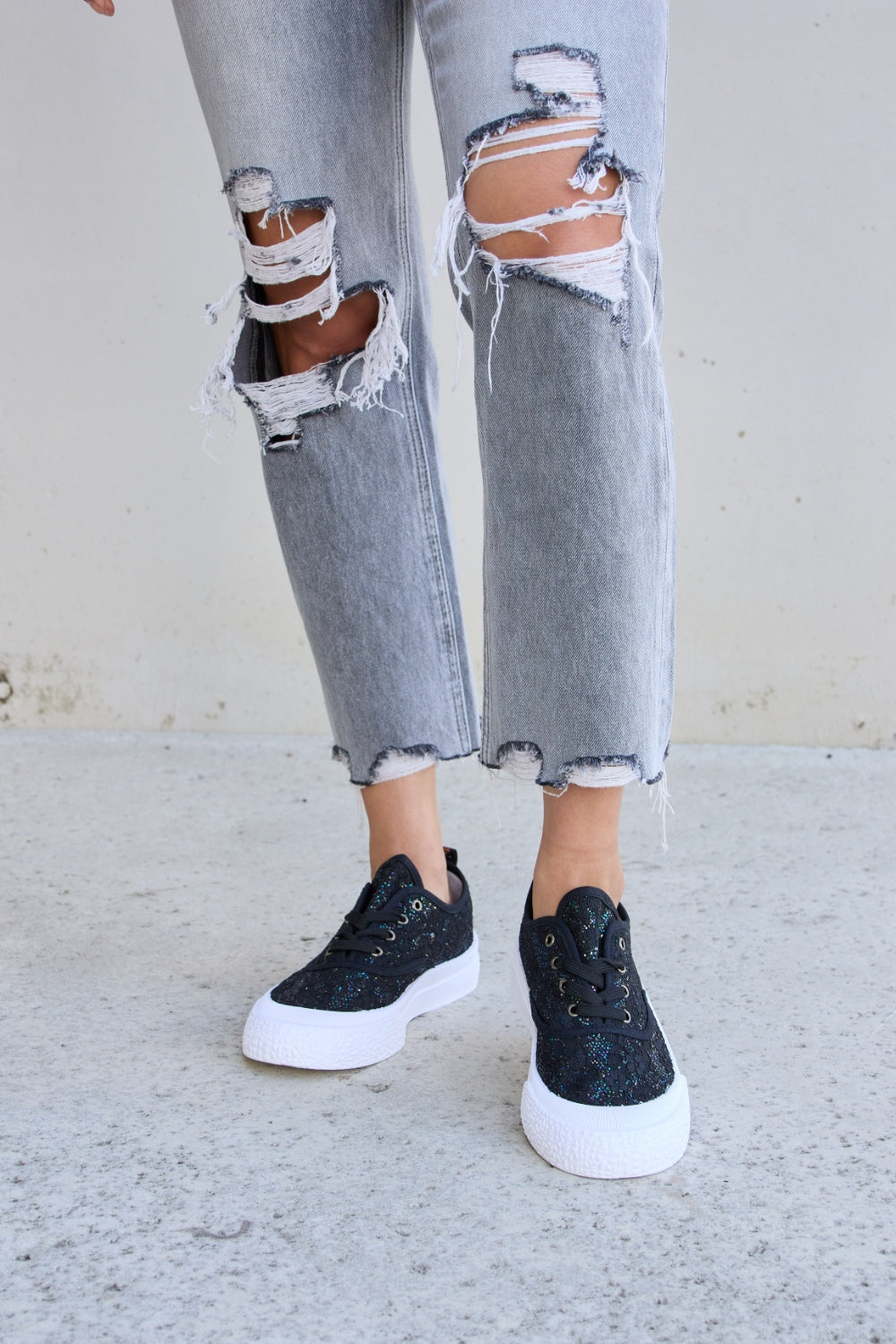 Person wearing ripped gray jeans and Forever Link Sequin Lace-Up Platform Sneakers.