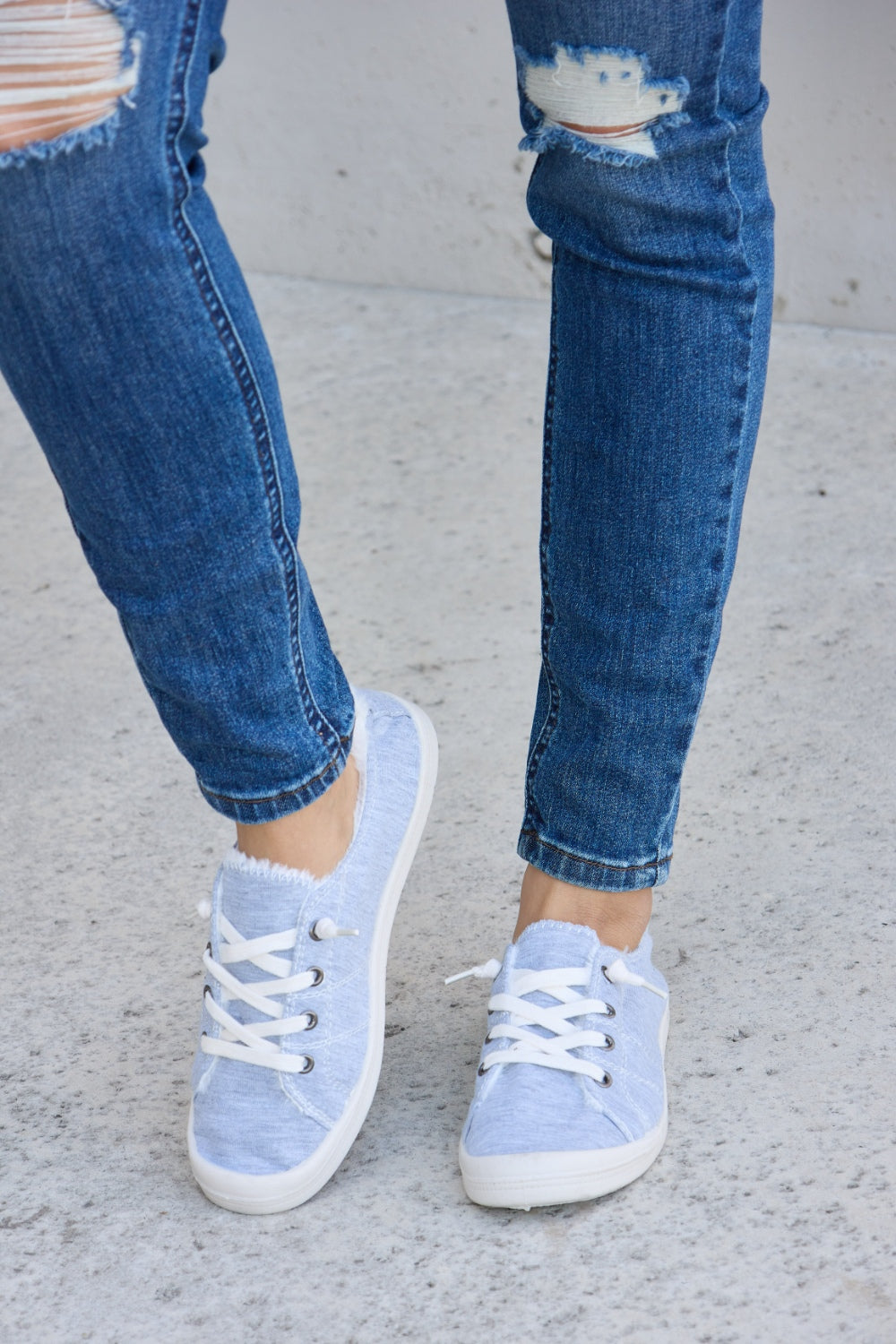 Person wearing ripped blue jeans and Forever Link Lace-Up Plush Thermal Flat Sneakers in grey with white laces, standing on a concrete surface.