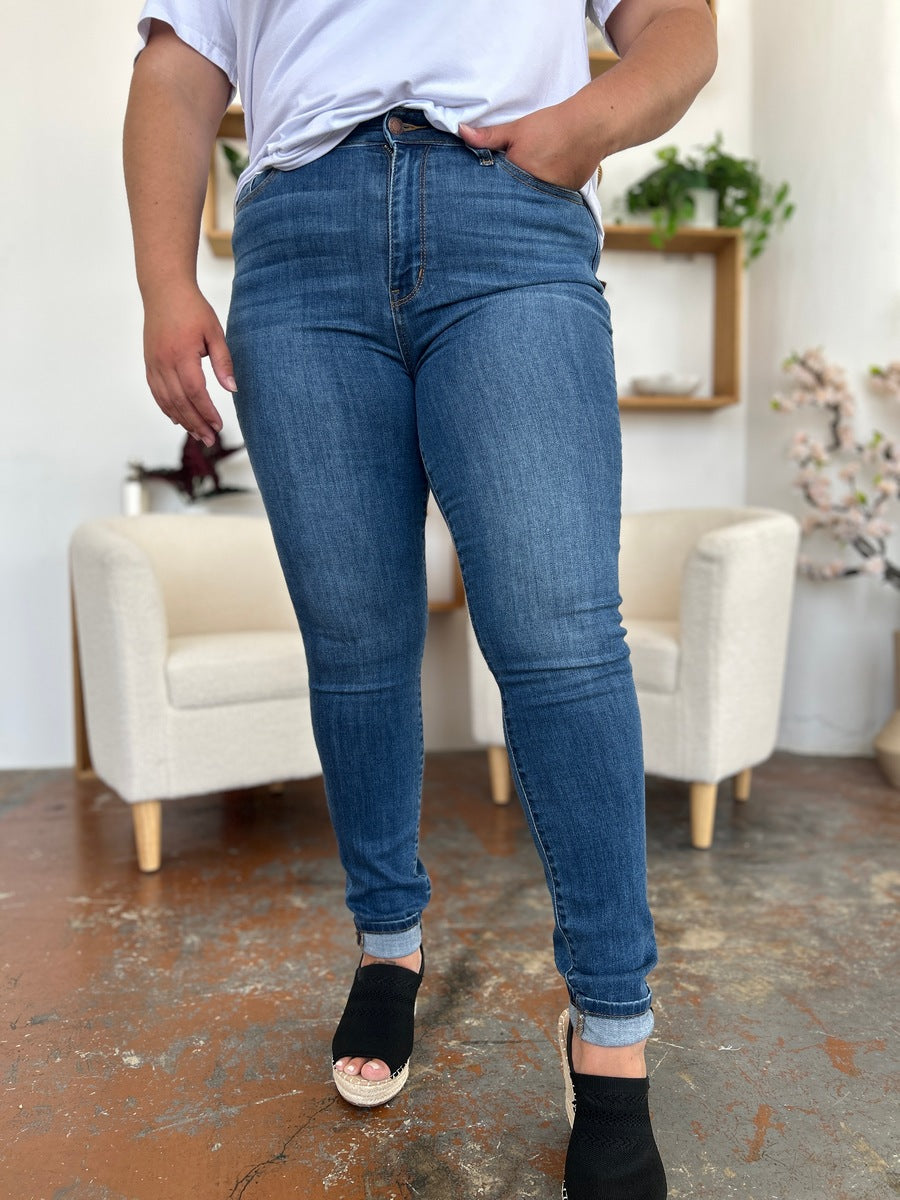 Person wearing Judy Blue Full Size Cuffed Hem Skinny Jeans and a white T-shirt, posing with one hand in pocket and feet in black open-toe shoes.