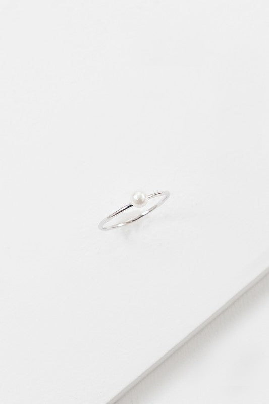 The "Single Pearl Ring," crafted from sterling silver with a single small pearl, rests on a white surface, embodying elegance in its design.