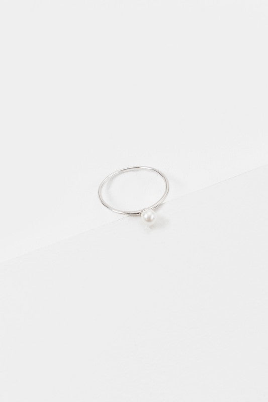 The "Single Pearl Ring," crafted from sterling silver with a single small pearl, rests on a white surface, embodying elegance in its design.