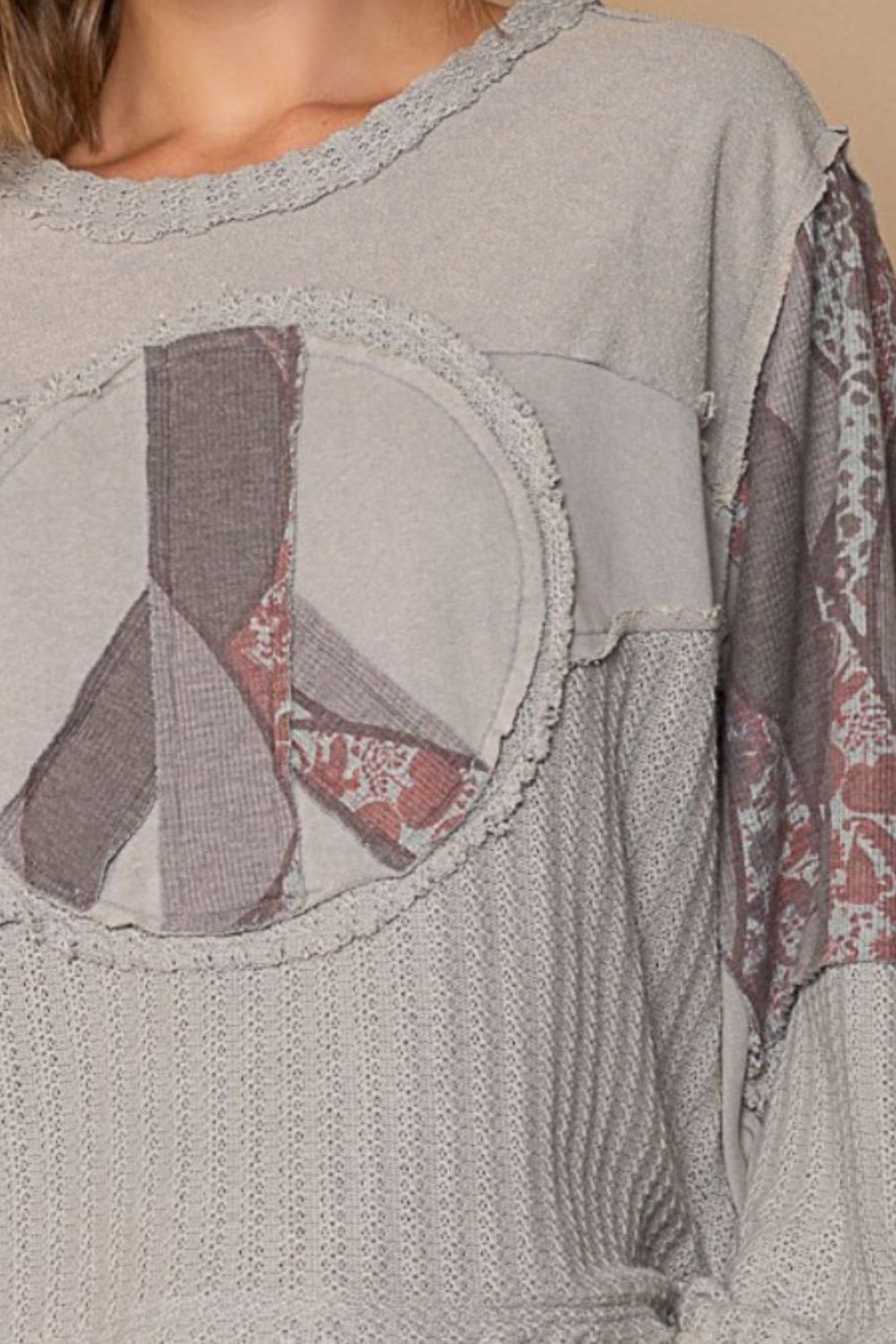 Young woman wearing a POL Long Sleeve Cut Sew Peace Emblem Top featuring a large peace sign design paired with beige shorts, standing against a plain background.