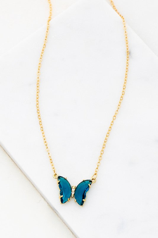 The Gem Stone Butterfly Pendant Necklace, available in an assortment of pastel hues and adorned with exquisite gemstone accents, is featured alongside matching earrings in shades of green, blue, pink, and clear, all elegantly displayed on a white surface.