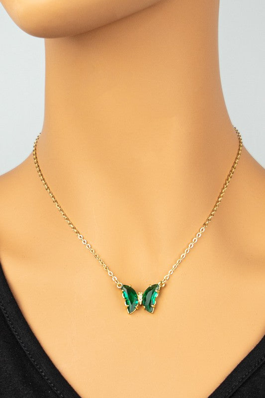 The Gem Stone Butterfly Pendant Necklace, available in an assortment of pastel hues and adorned with exquisite gemstone accents, is featured alongside matching earrings in shades of green, blue, pink, and clear, all elegantly displayed on a white surface.