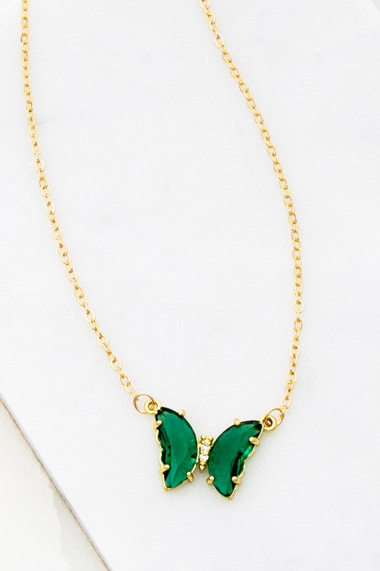 The Gem Stone Butterfly Pendant Necklace, available in an assortment of pastel hues and adorned with exquisite gemstone accents, is featured alongside matching earrings in shades of green, blue, pink, and clear, all elegantly displayed on a white surface.