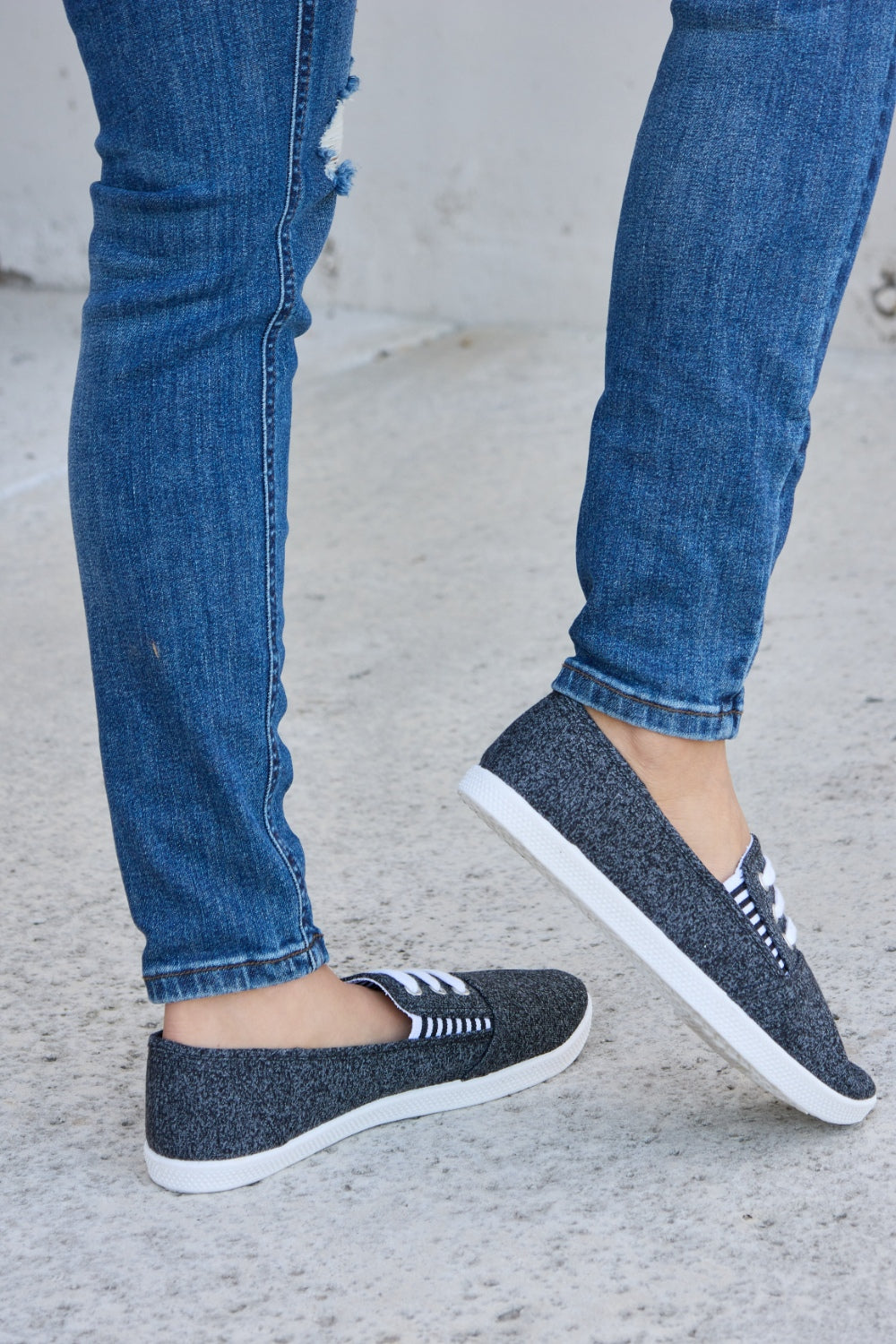 A person wearing ripped blue jeans and the fashionable Forever Link Round Toe Slip-On Flat Sneakers with white elastic bands.