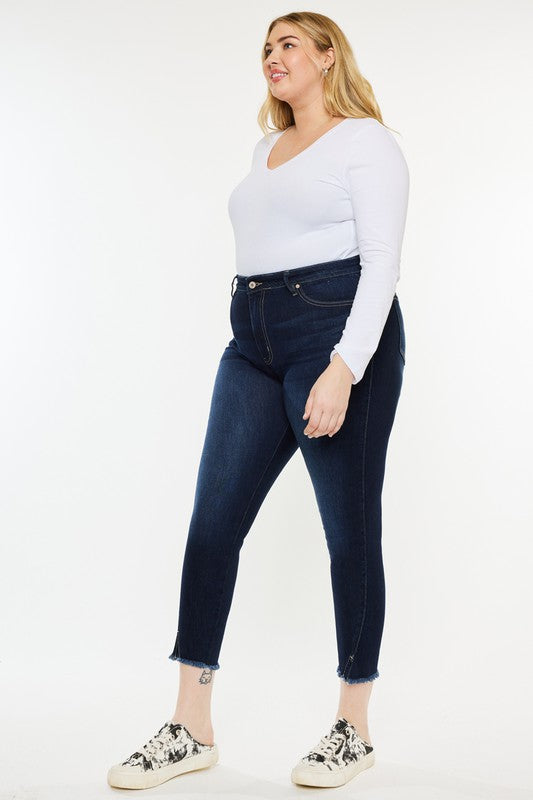 Woman wearing a white long-sleeve shirt, Plus High Rise Ankle Skinny Jeans in dark stone wash, and patterned sneakers stands against a plain white background.