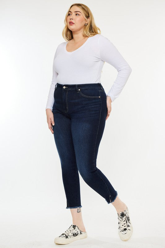 Woman wearing a white long-sleeve shirt, Plus High Rise Ankle Skinny Jeans in dark stone wash, and patterned sneakers stands against a plain white background.