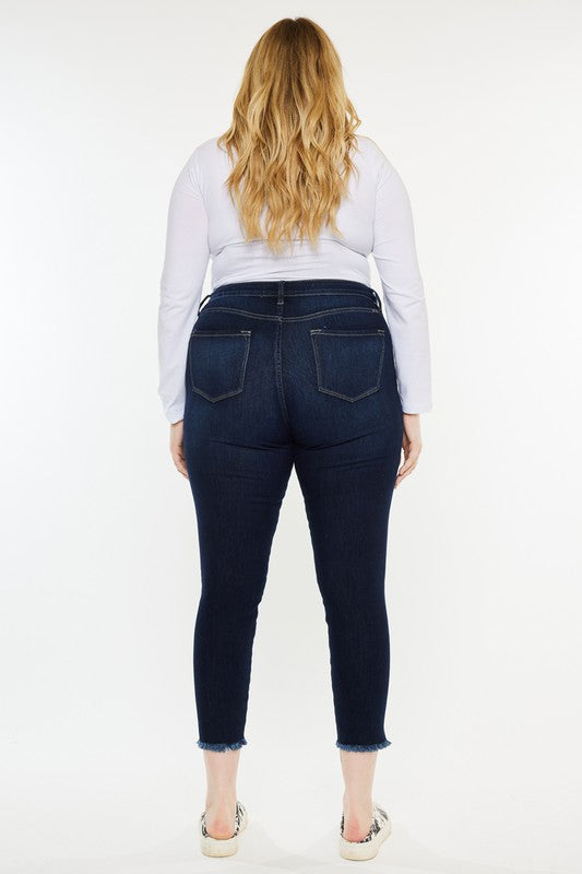 Woman wearing a white long-sleeve shirt, Plus High Rise Ankle Skinny Jeans in dark stone wash, and patterned sneakers stands against a plain white background.