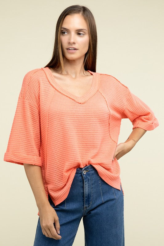 A person is dressed in a Brushed Waffle Exposed-Seam 3/4 Sleeve Top and white shorts, perfect for a casual wardrobe. They stand against a plain background, effortlessly embodying relaxed style.