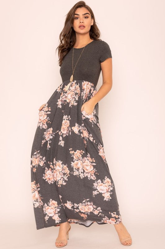 A woman wearing the Plus Short Sleeve Floral Maxi Dress stands smiling, her hands slightly above her waist, against a plain background. Made in the United States, her attire exudes charm and elegance.