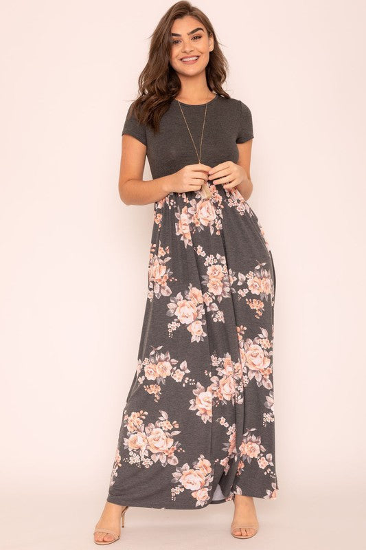 Against a plain backdrop, a woman is dressed in a Short Sleeve Floral Maxi Dress, which stylishly merges short sleeves with its elegant, flowing design.