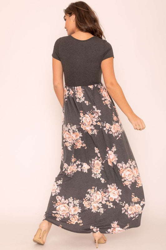 A woman wearing the Plus Short Sleeve Floral Maxi Dress stands smiling, her hands slightly above her waist, against a plain background. Made in the United States, her attire exudes charm and elegance.