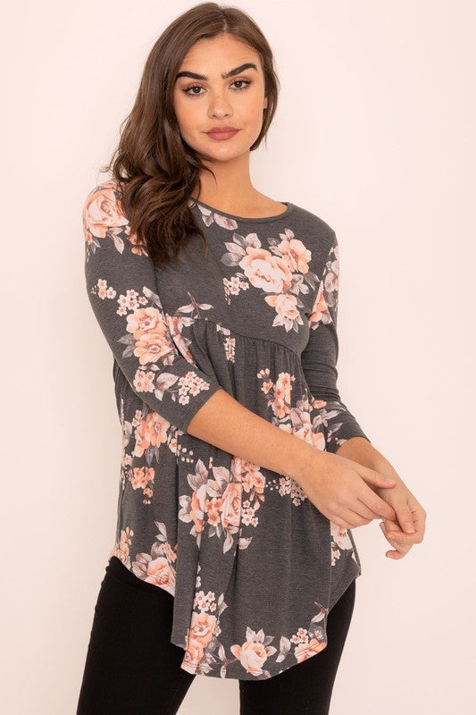 A woman wearing the Floral Curved Hem Tunic poses gracefully against a plain background, showcasing the elegant curved hem of her gray long-sleeved attire made in the United States.