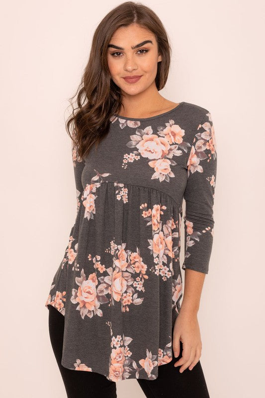 A woman wearing the Floral Curved Hem Tunic poses gracefully against a plain background, showcasing the elegant curved hem of her gray long-sleeved attire made in the United States.