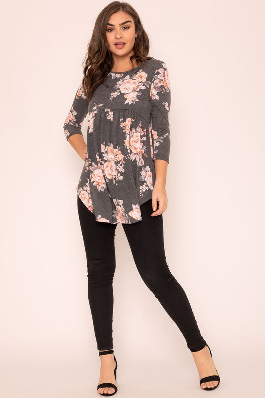 A woman wearing the Floral Curved Hem Tunic poses gracefully against a plain background, showcasing the elegant curved hem of her gray long-sleeved attire made in the United States.