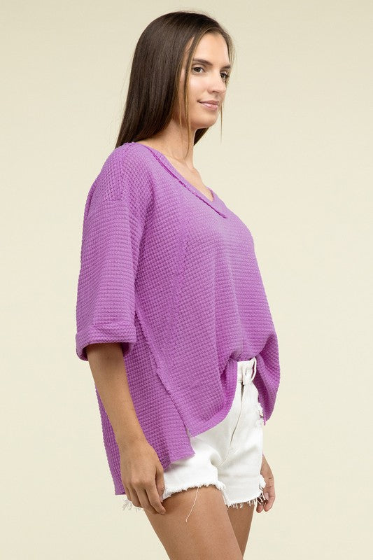 A person is dressed in a Brushed Waffle Exposed-Seam 3/4 Sleeve Top and white shorts, perfect for a casual wardrobe. They stand against a plain background, effortlessly embodying relaxed style.