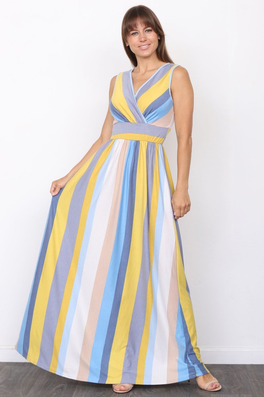 A person wearing the elegant Surplice Stripe Maxi Dress adorned with vertical pastel stripes in blue, pink, and white, stands gracefully on a wooden floor.