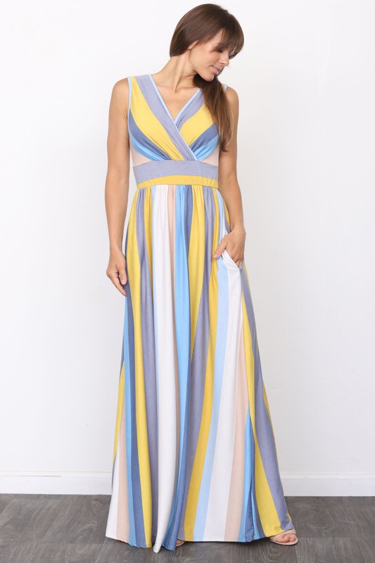 A person wearing the elegant Surplice Stripe Maxi Dress adorned with vertical pastel stripes in blue, pink, and white, stands gracefully on a wooden floor.