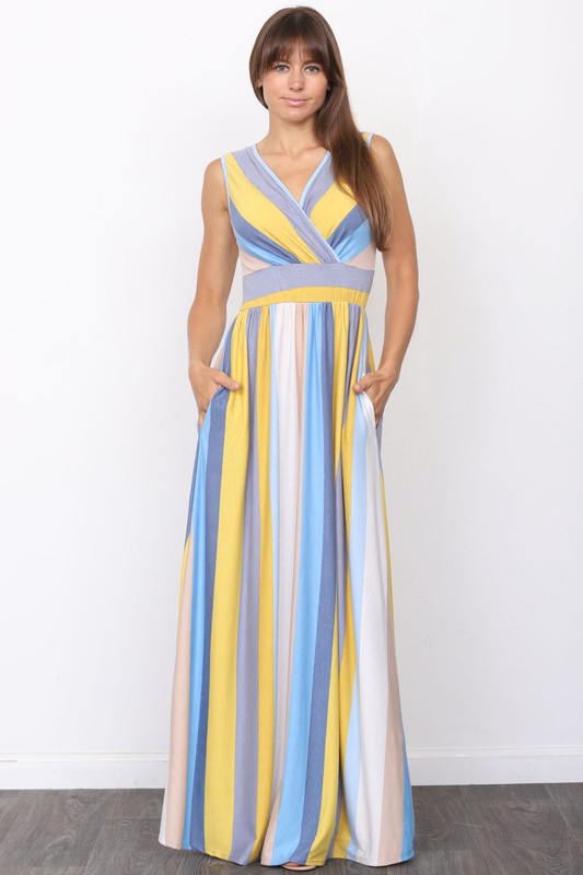 A person wearing the elegant Surplice Stripe Maxi Dress adorned with vertical pastel stripes in blue, pink, and white, stands gracefully on a wooden floor.