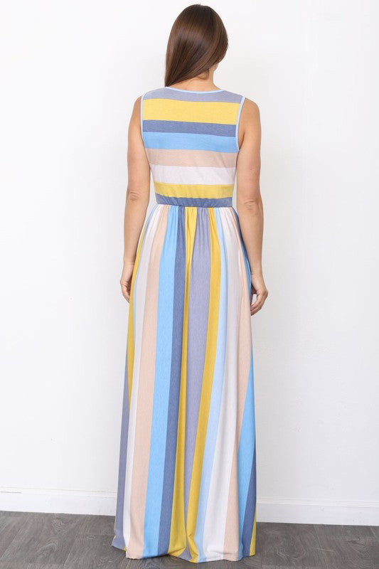 A person wearing the elegant Surplice Stripe Maxi Dress adorned with vertical pastel stripes in blue, pink, and white, stands gracefully on a wooden floor.