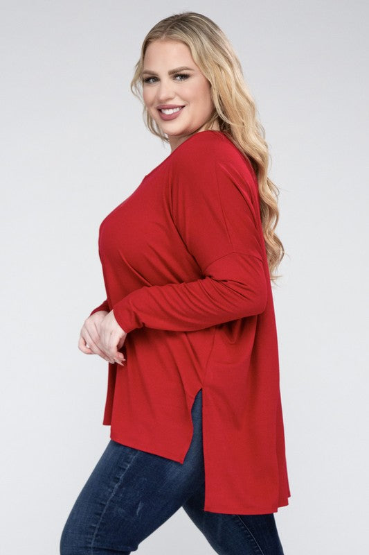 A woman with long, blonde hair wears a Plus Dolman Sleeve V-Neck Side Slit Hi-Low Hem Top and blue jeans, posing with one hand on her hip and smiling at the camera.