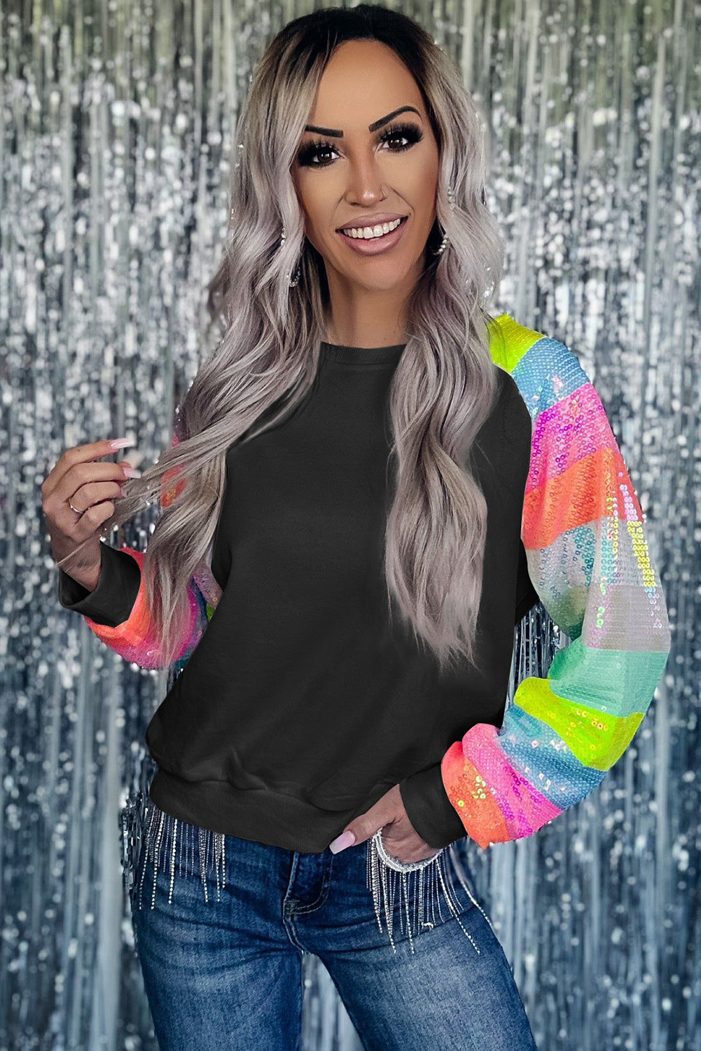 A person with shoulder-length hair is wearing a Black Sequin Color Block Raglan Sleeve Pullover Sweatshirt and blue jeans. They are facing away from the camera in a room with a potted plant.