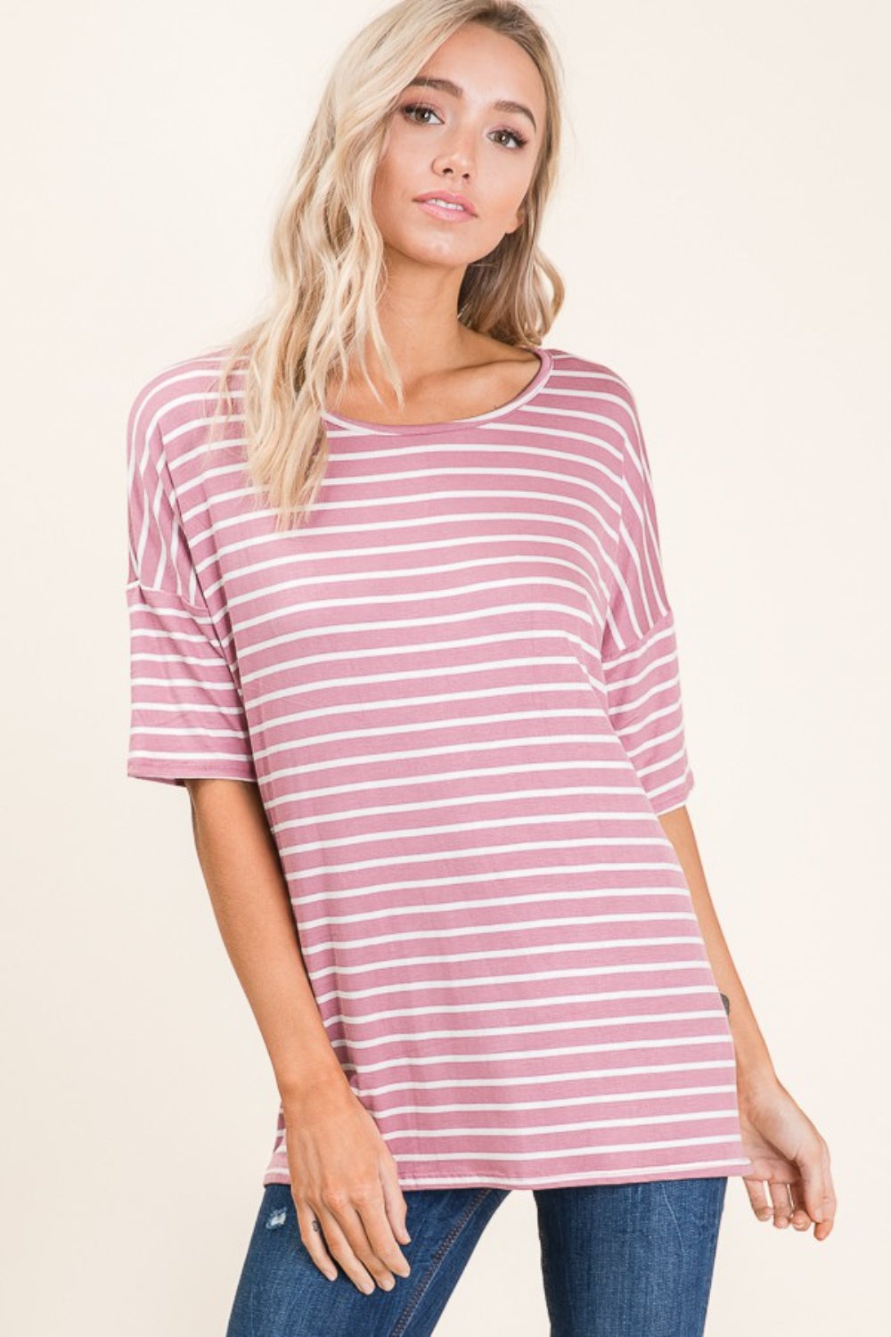 A person wearing a BOMBOM Striped Round Neck Half Sleeve T-Shirt in pink and white paired with blue jeans stands against a neutral background.