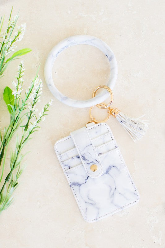 A person seated with a small black Key Ring Wallet Bracelets attached to their denim shorts, containing car keys and cash.