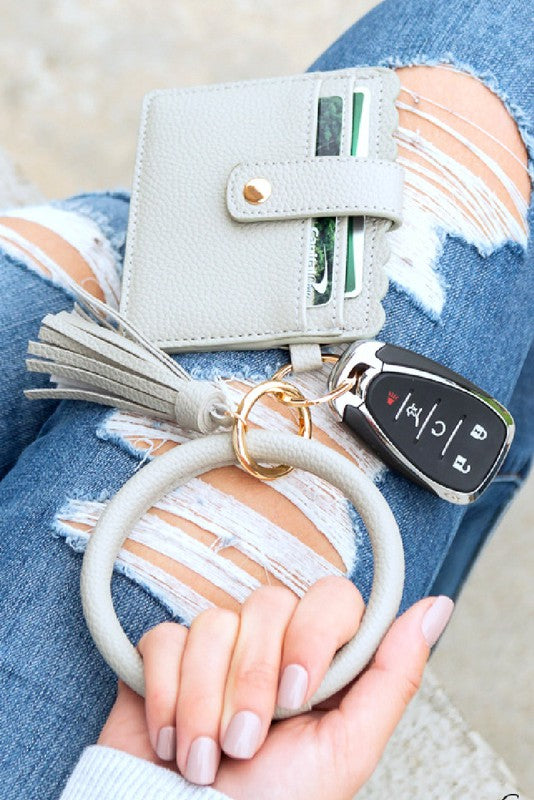 A person's lap with a Key Ring ID Wallet Bracelet featuring button snap closure, car keys on a key ring, and a hand with white nail polish.