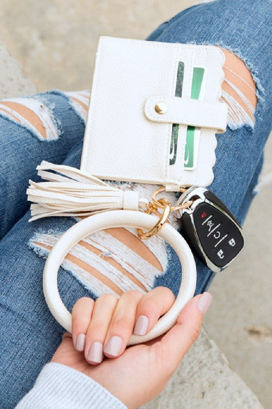 A person's lap with a Key Ring ID Wallet Bracelet featuring button snap closure, car keys on a key ring, and a hand with white nail polish.