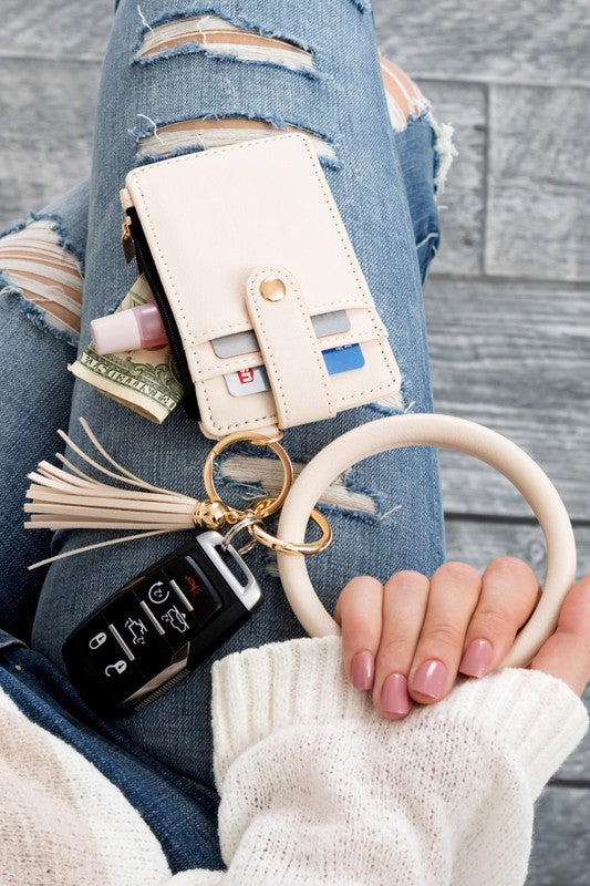 A person's hand holding a Key Ring Wallet Bracelet ID Zip Up with a leopard print design; cash and cards are partially visible inside the wallet, which features a hidden zipper pocket.