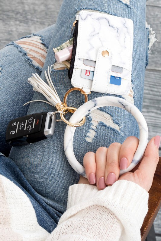 A person's hand holding a Key Ring Wallet Bracelet ID Zip Up with a leopard print design; cash and cards are partially visible inside the wallet, which features a hidden zipper pocket.