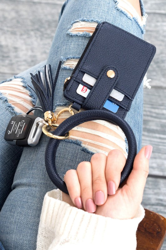 A person's hand holding a Key Ring Wallet Bracelet ID Zip Up with a leopard print design; cash and cards are partially visible inside the wallet, which features a hidden zipper pocket.