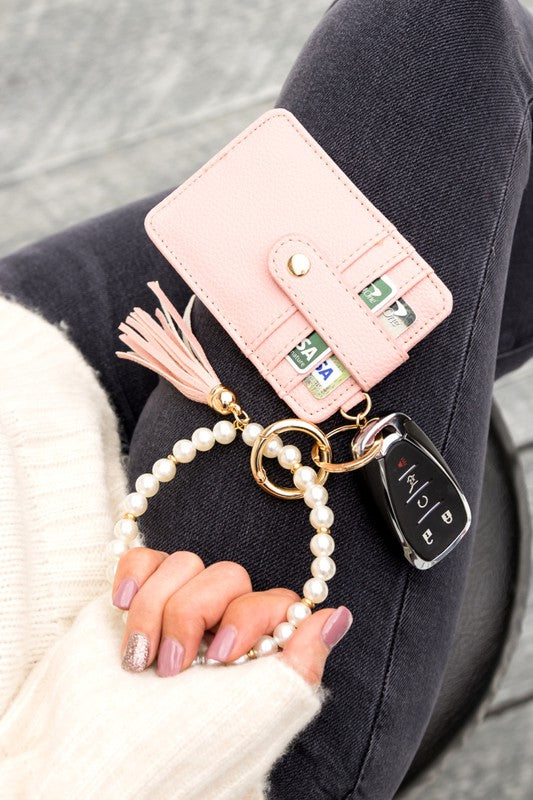 A person holding a Pearl Key Ring Wallet Bracelet with a vegan leather tassel and car keys attached.