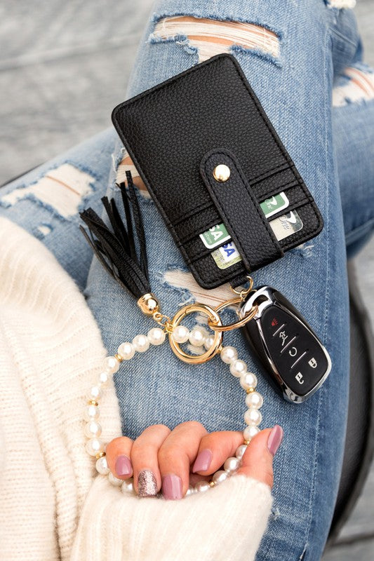 A person holding a Pearl Key Ring Wallet Bracelet with a vegan leather tassel and car keys attached.