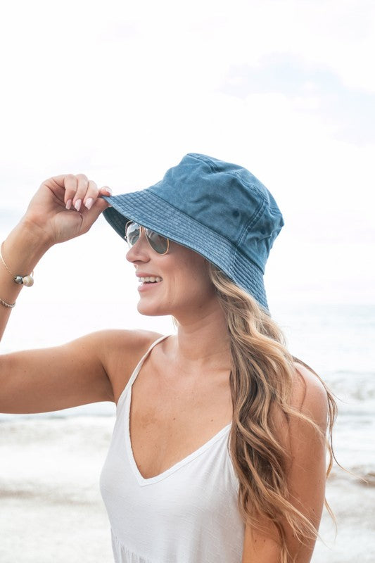 Woman holding a Solid Distressed Bucket Hat, wearing sunglasses at the beach.