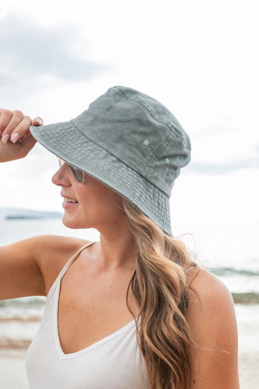 Woman holding a Solid Distressed Bucket Hat, wearing sunglasses at the beach.