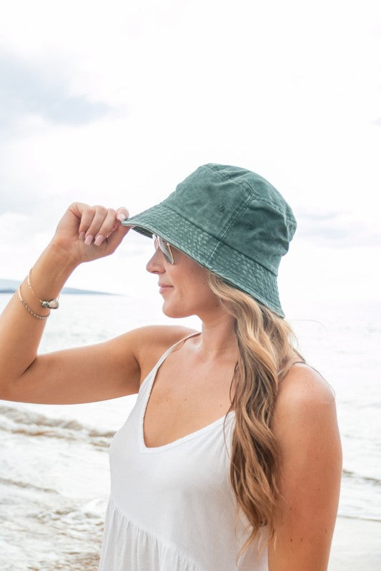 Woman holding a Solid Distressed Bucket Hat, wearing sunglasses at the beach.