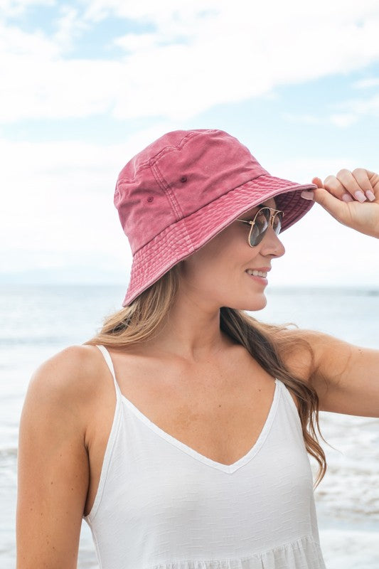 Woman holding a Solid Distressed Bucket Hat, wearing sunglasses at the beach.