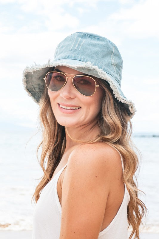 Woman wearing sunglasses and a Levi's Denim Bucket Hat with a frayed edge at the beach.