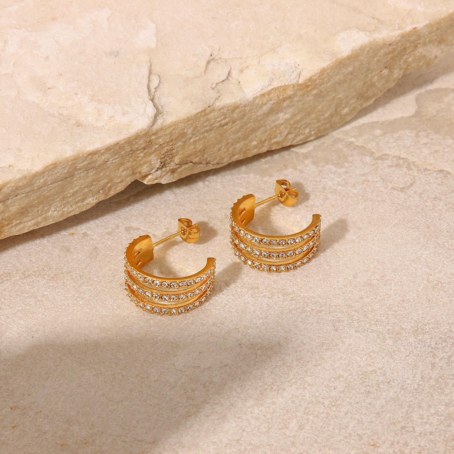 The Stainless Steel Inlaid Zircon C-Hoop Earrings perfectly blend elegance, featuring a triple row of small, clear gemstones on each gold-plated hoop.