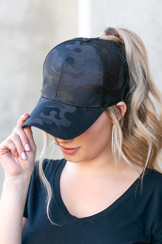 Woman wearing a black Camo Messy Bun Cap with an adjustable Velcro closure.