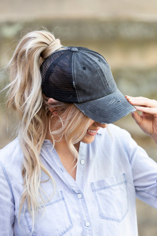 Woman smiling and tipping her gray, Distressed Messy Bun Hat Cap.