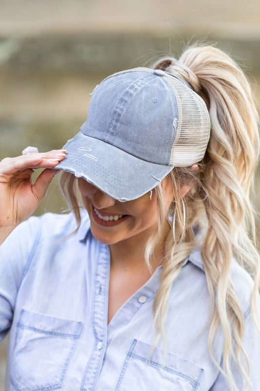 Woman smiling and tipping her gray, Distressed Messy Bun Hat Cap.
