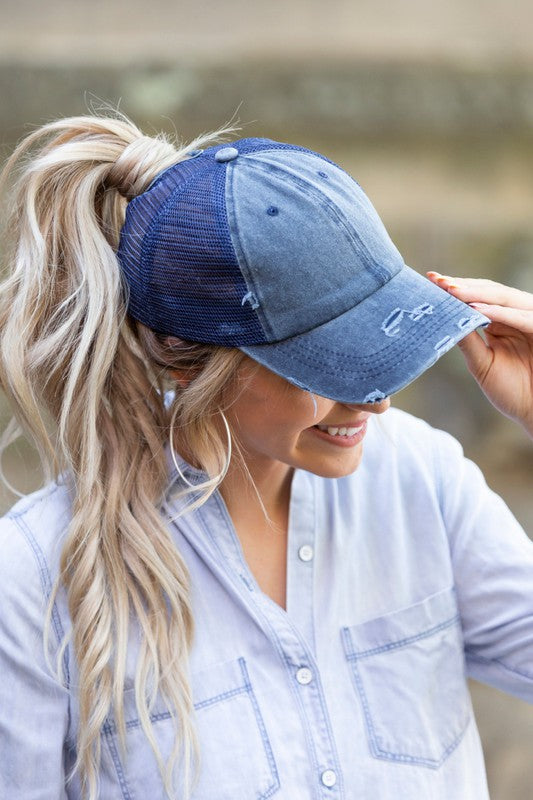 Woman smiling and tipping her gray, Distressed Messy Bun Hat Cap.