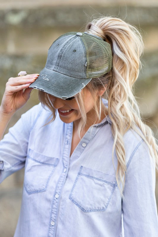 Woman smiling and tipping her gray, Distressed Messy Bun Hat Cap.