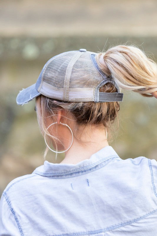 Woman smiling and tipping her gray, Distressed Messy Bun Hat Cap.